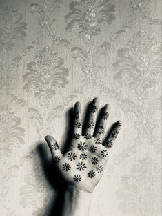 a person's hand with black and white flowers painted on the palm, against a wallpapered background