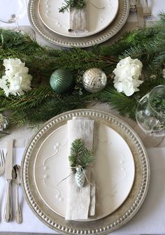 the table is set for christmas dinner with pine cones and silverware, greenery and ornaments