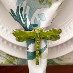 a green dragonfly sitting on top of a white plate next to a flower covered napkin