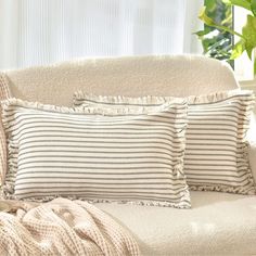 two pillows sitting on top of a white couch next to a potted green plant