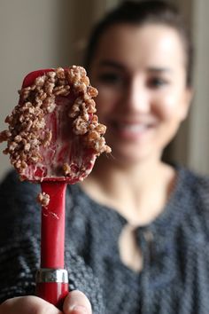 a woman holding up a red object with some food on it's tip and smiling at the camera