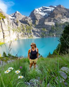 a woman standing on top of a lush green hillside next to a lake with mountains in the background