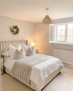 a white bed sitting next to a window in a bedroom on top of a carpeted floor