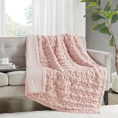 a pink blanket sitting on top of a couch next to a potted plant