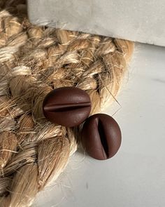 two brown buttons sitting on the side of a piece of braided fabric next to a white wall