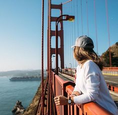 a woman standing on the side of a bridge looking out at the water and hills