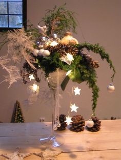 a glass vase filled with pine cones and greenery on top of a wooden table