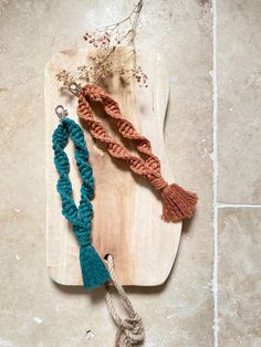 two necklaces on a wooden board next to a flower and roped cord hanging from it