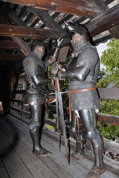 two men dressed in armor standing next to each other on a wooden platform with trees in the background