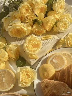 yellow roses and croissants are on the table with lemons, oranges and bread