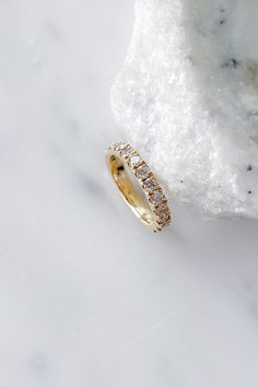 a gold ring with two rows of diamonds on top of a marble slab in front of a rock