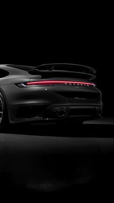 the rear end of a black porsche sports car in a dark room with its lights on