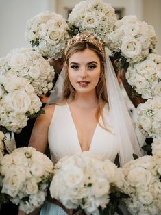 a woman standing in front of a wreath with flowers on it and wearing a wedding dress