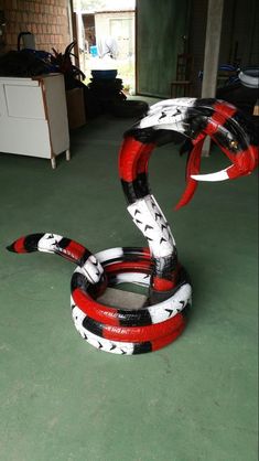 a red, black and white snake sculpture sitting on the ground in a room with green flooring