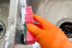 a person in orange gloves is cleaning a sink with a sponge and soap on it