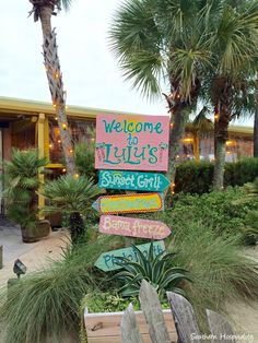 a sign that is on the side of a wooden fence in front of some palm trees