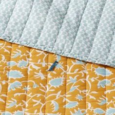 an orange and blue quilted bed spread with white flowers on the bottom, along with a light blue pillow