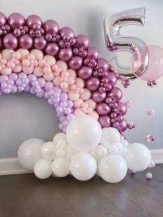 balloons are floating in the air next to a large number 5 balloon arch that is decorated with pink, purple and white balloons