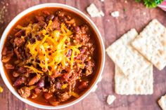 a bowl filled with chili and cheese next to crackers