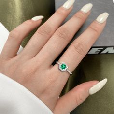 a woman's hand with white nails and an emerald ring