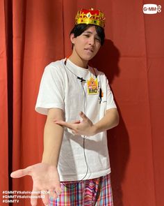 a young man wearing a crown on top of his head while standing in front of a red curtain