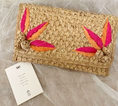 a straw purse with pink and orange leaves on it next to a card holder that has a note attached