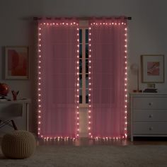 a pink curtain with lights on it in a room next to a dresser and chair