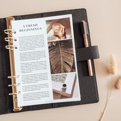 an open planner book on top of a desk next to a pen and some dried flowers