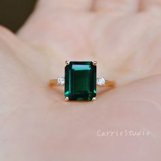 an emerald and diamond ring sitting on someone's hand