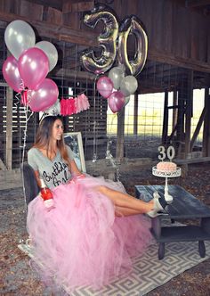 a woman in a pink dress sitting on a chair with balloons and decorations around her