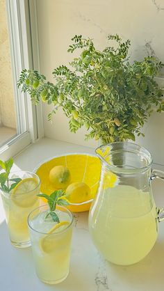 lemonade and water are sitting on a table next to a pitcher, bowl, and glassware