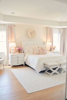 a white bed sitting in a bedroom on top of a hard wood floor next to two windows