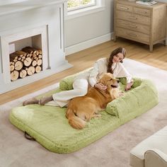 a woman sitting on top of a dog bed next to a fire place