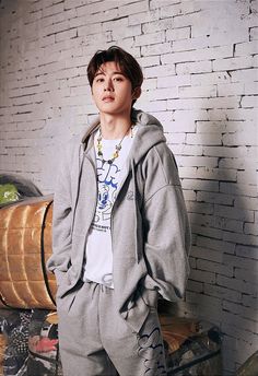 a young man standing in front of a brick wall wearing a hoodie and sweatpants