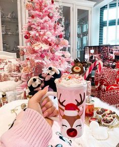 a person holding a cup in front of a pink christmas tree with ornaments on it