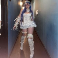 a woman with blue hair and white dress walking down a hallway wearing knee high boots