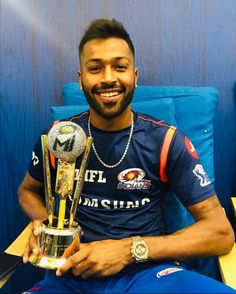 a man sitting on a blue couch holding a trophy and two silver balls in his hands