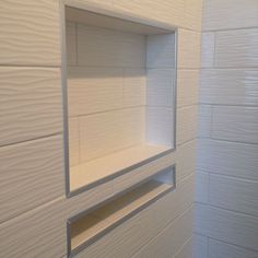 an empty shelf in the corner of a white tiled room with light coming through it