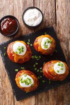 four small pastries with sour cream and chives on a black slate platter