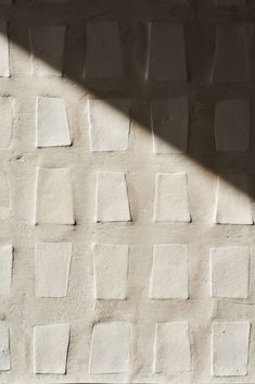 a white brick wall with small squares on it and a shadow cast by the light