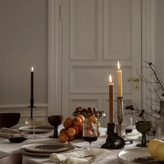 a table set with plates, candles and fruit on it in front of a white wall