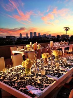 an outdoor dining area with tables and chairs set up for dinner at dusk, overlooking the city skyline