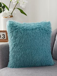 a blue pillow sitting on top of a gray couch next to a vase with flowers