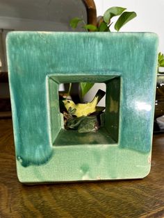 a green square shaped vase with a yellow bird in it