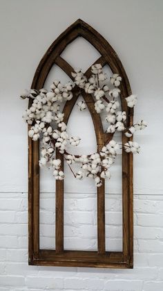 a wooden window frame with cotton flowers hanging on it's side, against a white brick wall