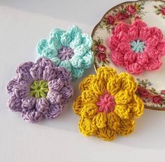 four crocheted flowers are on a plate next to each other in different colors