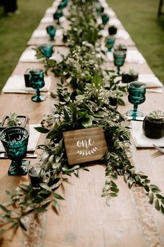 a long table with place settings and greenery