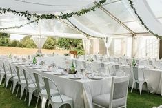 tables and chairs are set up in a tent for an outdoor wedding or party with white linens and greenery hanging from the ceiling