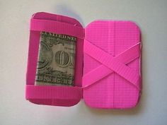 an origami cell phone is wrapped in pink paper and has a dollar bill sticking out of it