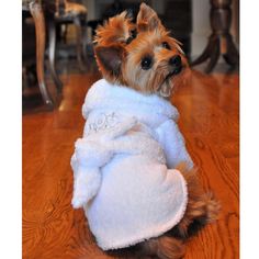 a small dog wearing a white robe on top of a wooden floor next to a table